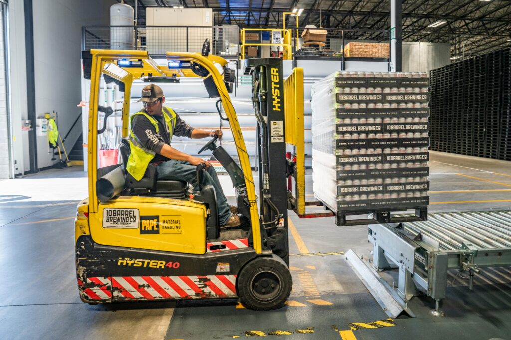 pexels-photo-1267338-1267338 A warehouse worker maneuvers a forklift to transport crates for brewing company storage.